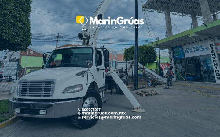 Grúa Titán estabilizada durante el montaje de un poste metálico en una zona comercial.