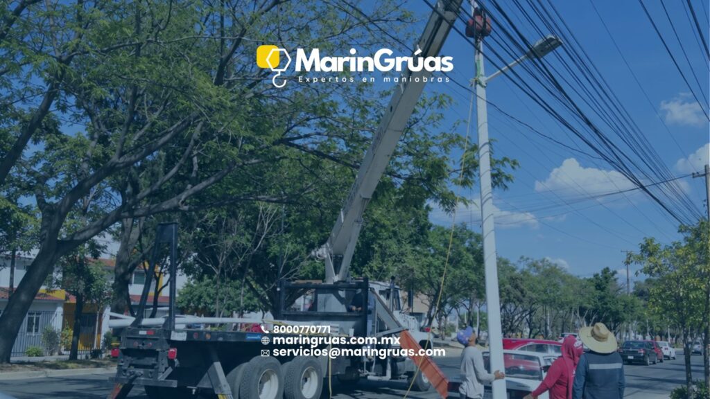Grúa Titán instalando un poste de alumbrado en vía pública, cerca de cableado aéreo.