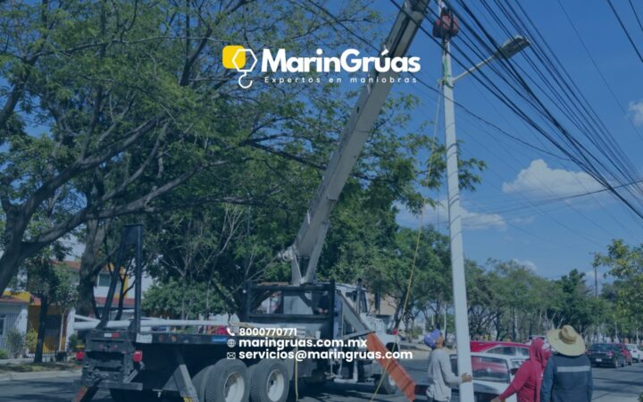 Grúa Titán instalando un poste de alumbrado en vía pública, cerca de cableado aéreo.
