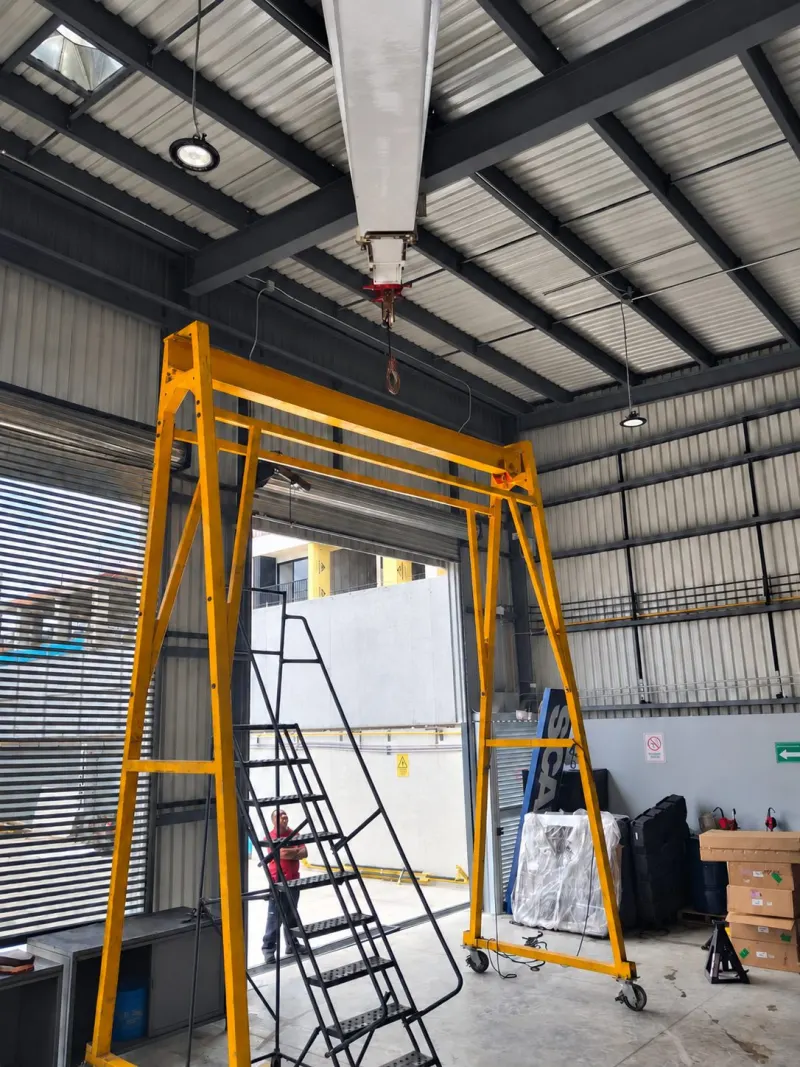Pluma de grúa dentro de la nave, sobre una estructura metálica amarilla con ruedas.