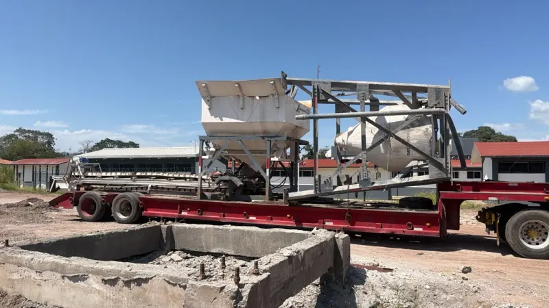 Báscula con banda transportadora y depósito superior sobre terreno de tierra, con montañas al fondo.