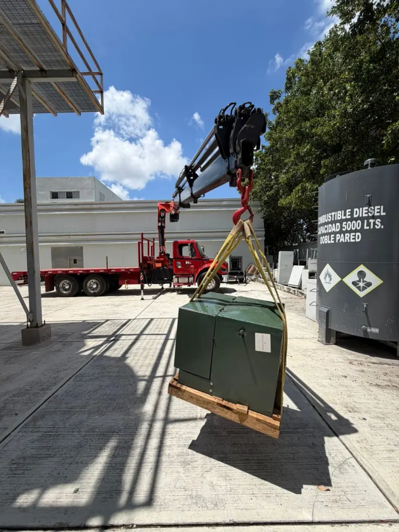 Camión con grúa HIAB roja y transformador sobre la plataforma frente a un edificio industrial.