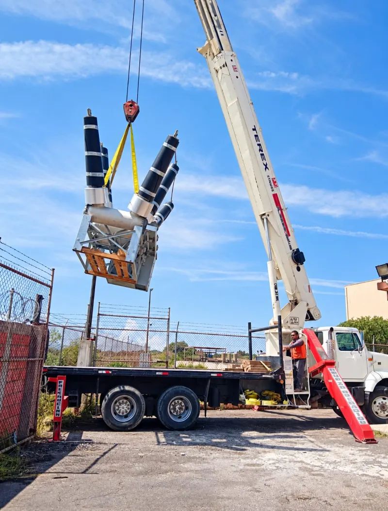Grúa Titán eleva un equipo eléctrico de tres polos sobre una malla con alambre de seguridad.