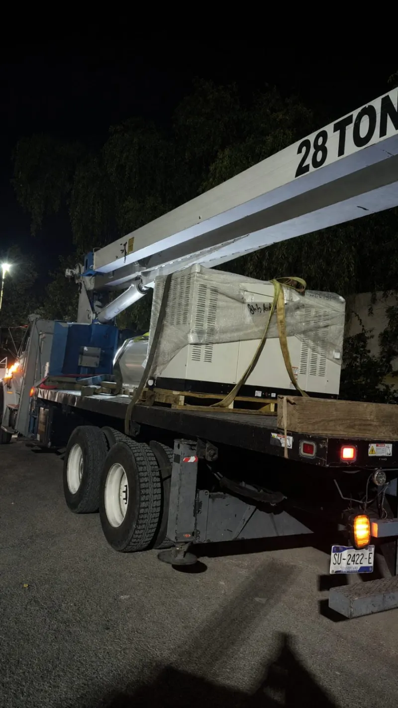 Planta eléctrica envuelta y asegurada sobre la plataforma de una grúa Titán durante la noche.