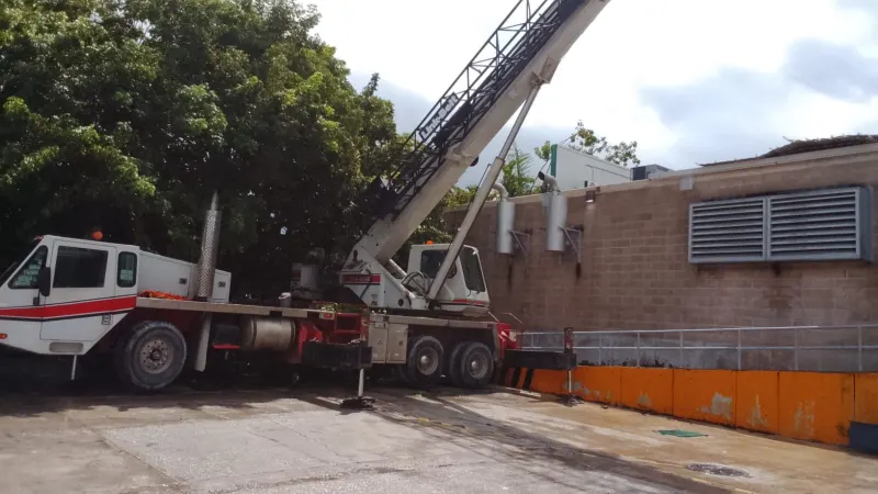 Grúa telescópica estabilizada en un patio angosto entre árboles y el muro de una nave en un CEDIS de Campeche