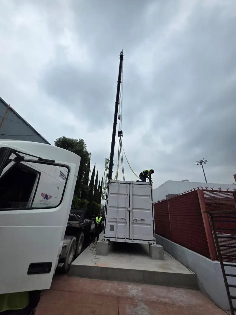 Extremo con puertas de un contenedor suspendido sobre apoyos de concreto, con una persona en la parte superior.