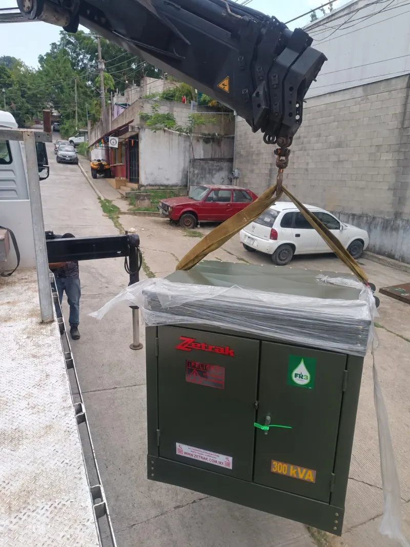 Equipo eléctrico elevado con eslingas mientras una persona controla una cuerda guía.