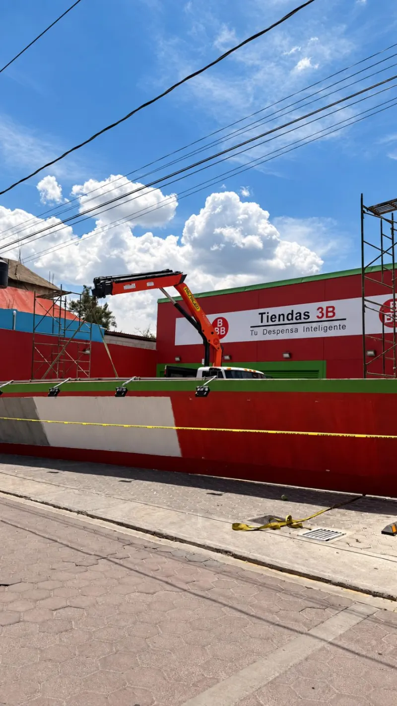 Pluma articulada roja, andamios y líneas aéreas frente a la fachada de una tienda.