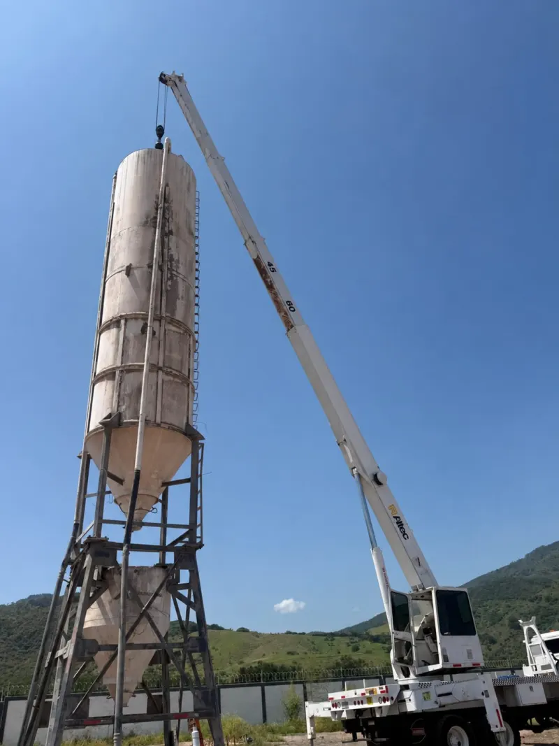 Grúa Titán blanca con la pluma extendida sobre un silo vertical montado en una estructura metálica.