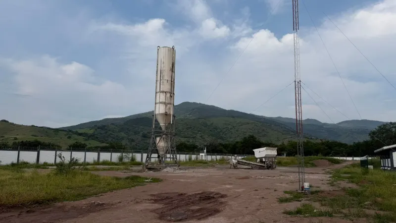 Silo vertical en una zona agrícola, rodeado de terreno de tierra, equipos y montañas.
