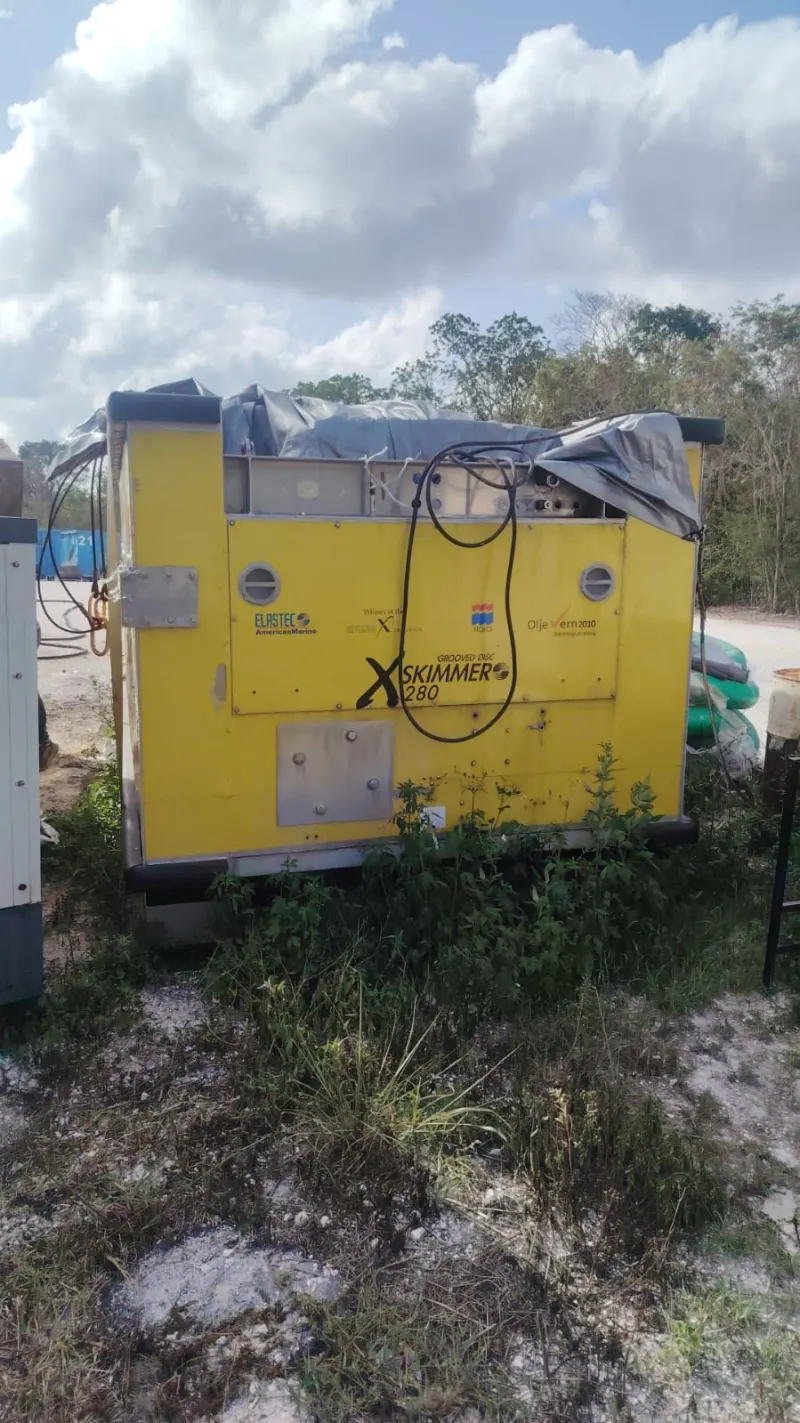 Unidad de potencia hidráulica con gabinete abierto, controles visibles y el skimmer amarillo al fondo.