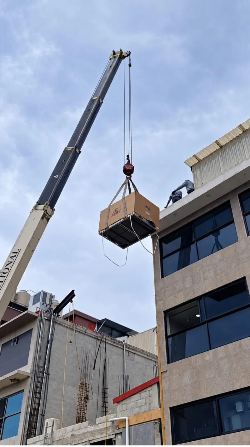 Camión grúa Titán en un acceso estrecho, con estabilizadores desplegados junto al edificio.
