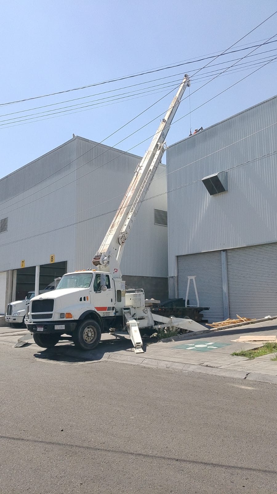 Grúa Titán estabilizada frente a una nave, con la pluma elevada entre cableado aéreo.