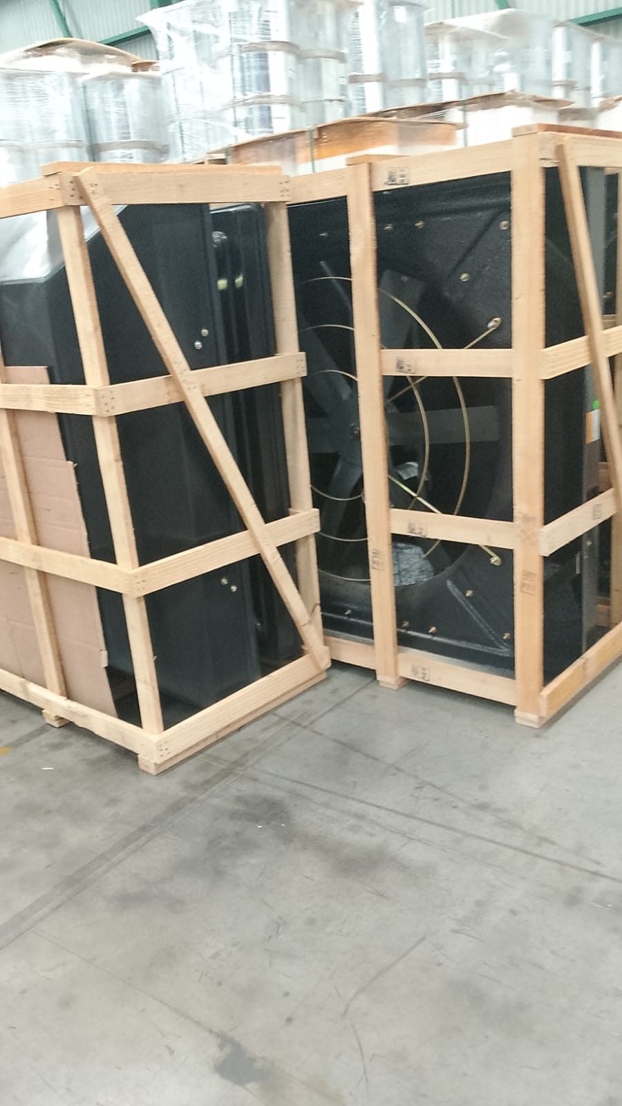 Equipos extractores negros dentro de bastidores de madera, almacenados en una nave industrial.