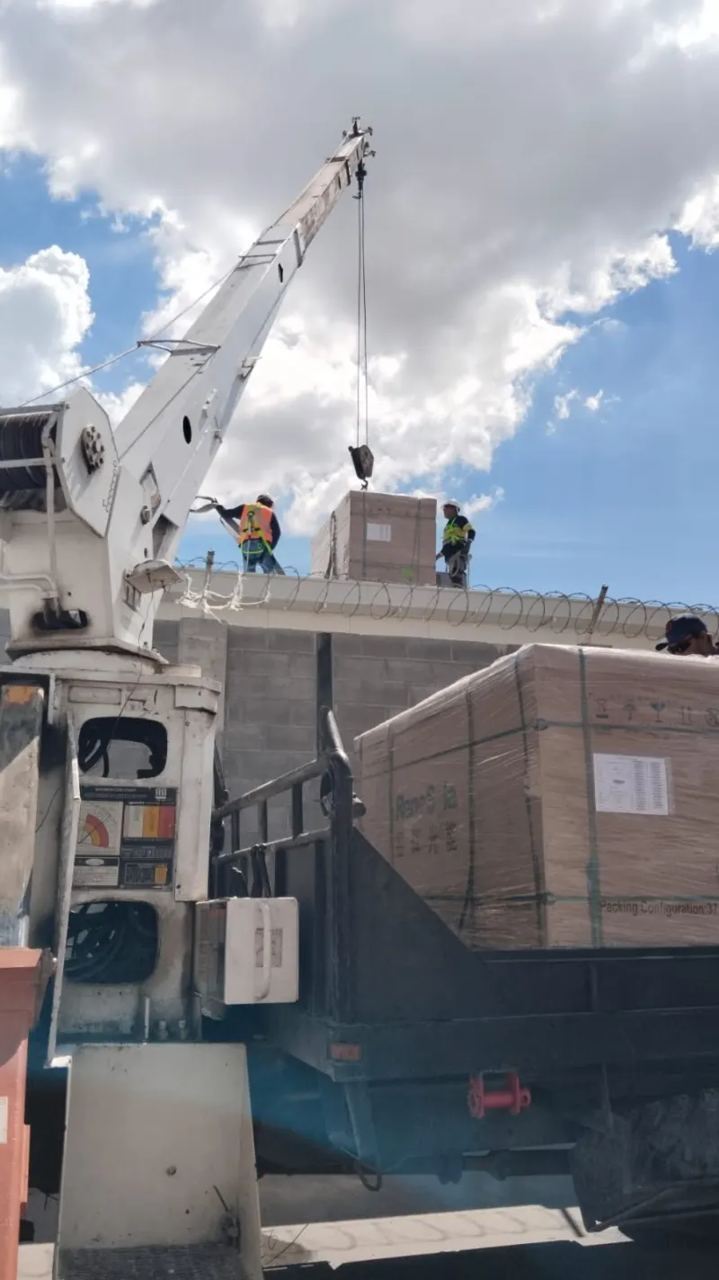 Caja de módulos sobre la cubierta junto a personal con chalecos; otra tarima permanece sobre el camión.