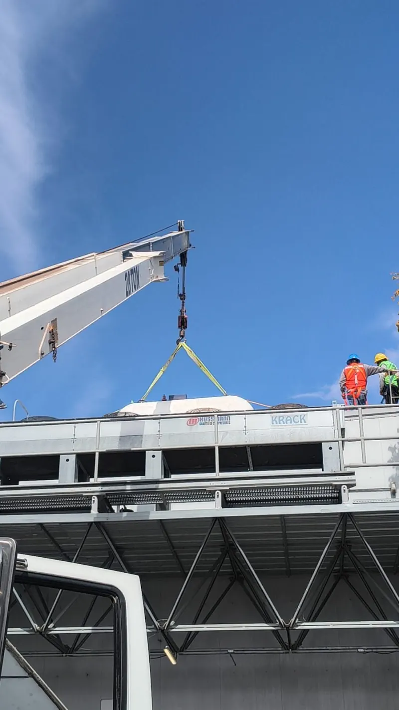 Grúa Titán elevando un equipo de aire acondicionado hacia una plataforma con trabajadores.