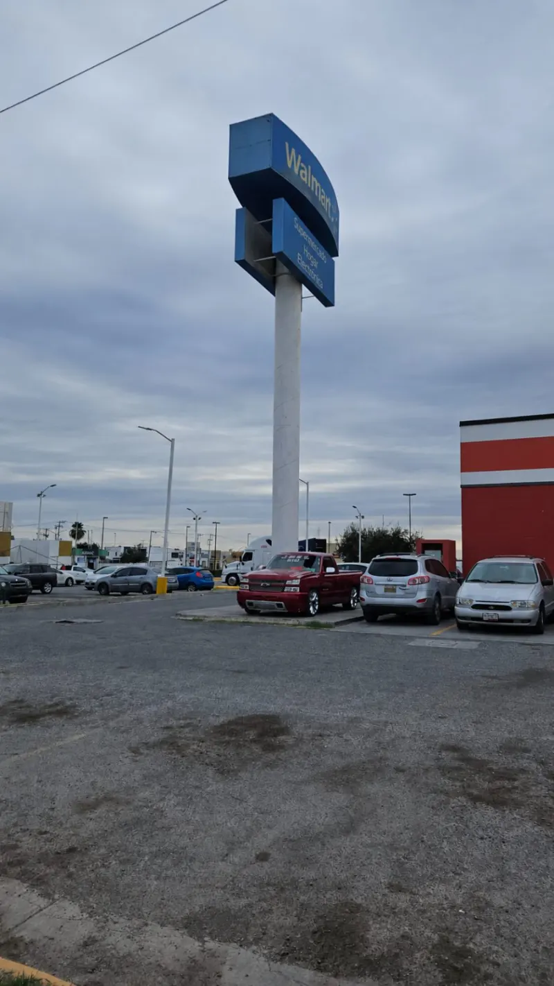 Tótem azul con poste blanco, escalera vertical y vehículos estacionados alrededor.