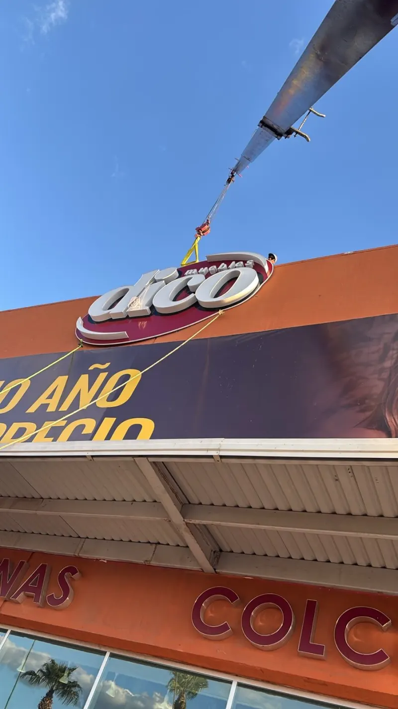 Grúa Titán en el estacionamiento frente a una tienda; el anuncio oval cuelga junto a la parte alta de la fachada.