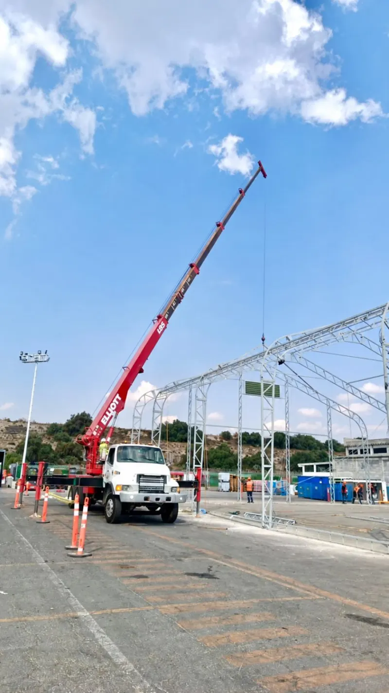 Grúa articulada roja con la pluma extendida sobre una estructura metálica curva.