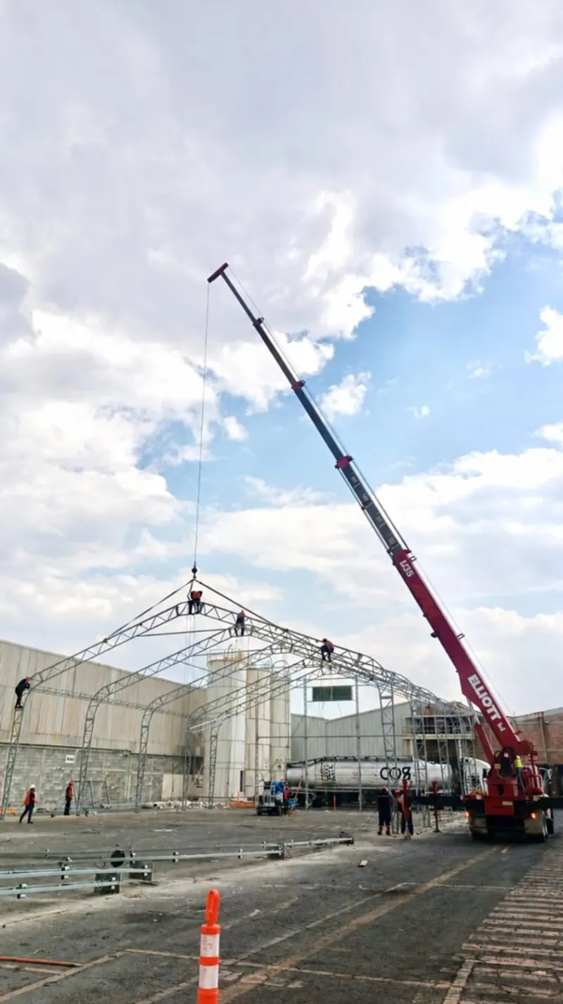 Personal guía una cercha suspendida sobre los arcos de una cubierta industrial.