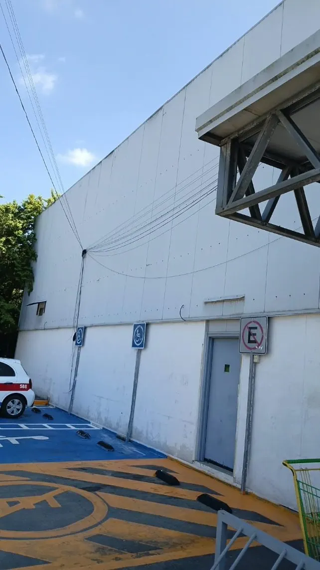 Paquete HVAC suspendido por una grúa sobre el estacionamiento, con un trabajador en el borde de la azotea.