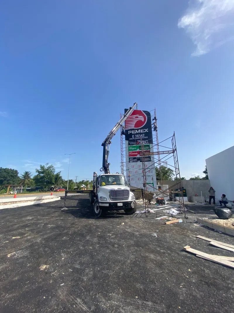 Vista amplia de la grúa HIAB y el andamio frente a la estructura tipo tótem en montaje.