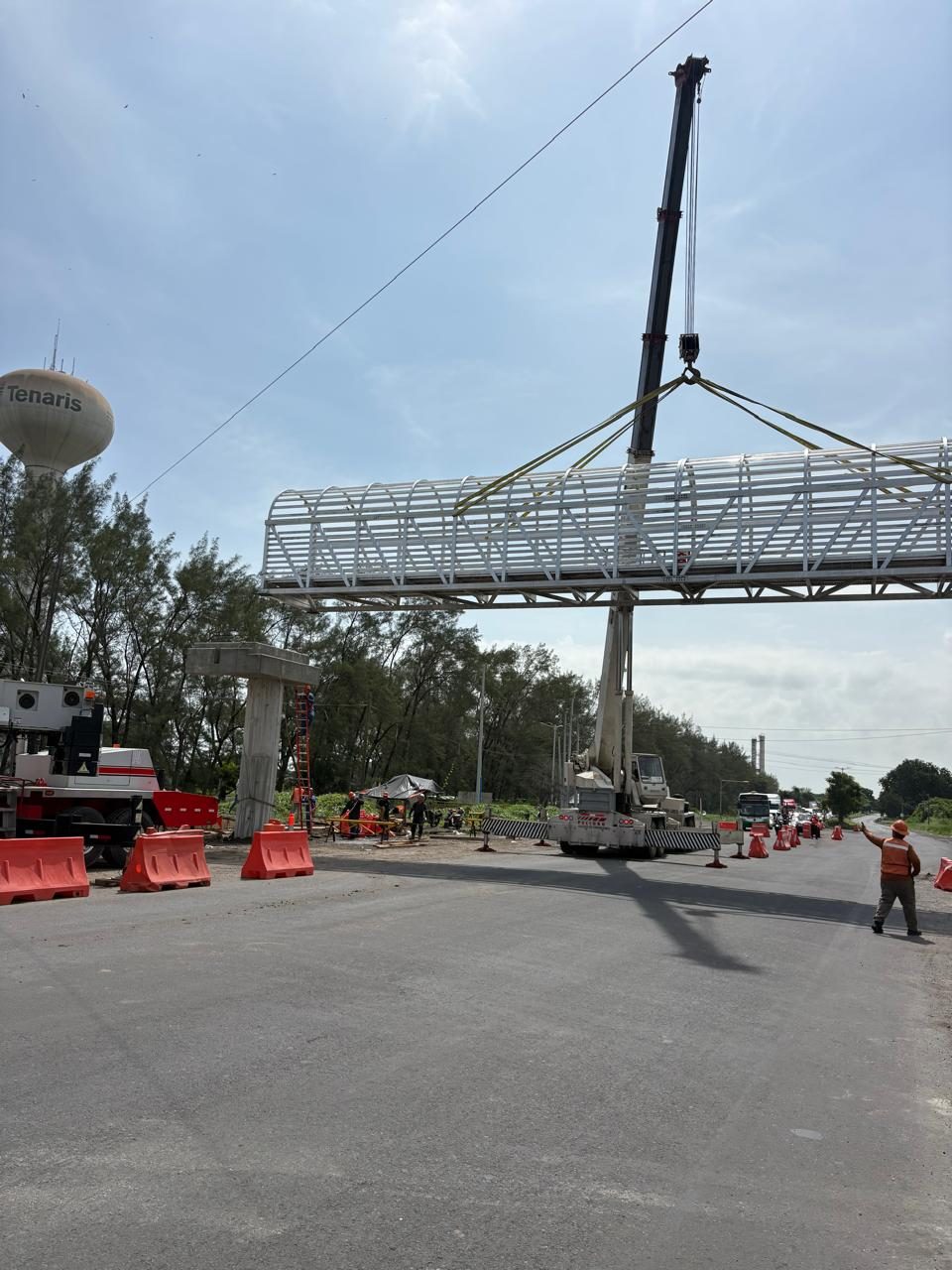 Puente de aluminio suspendido por eslingas sobre la vía, con una grúa telescópica al centro.