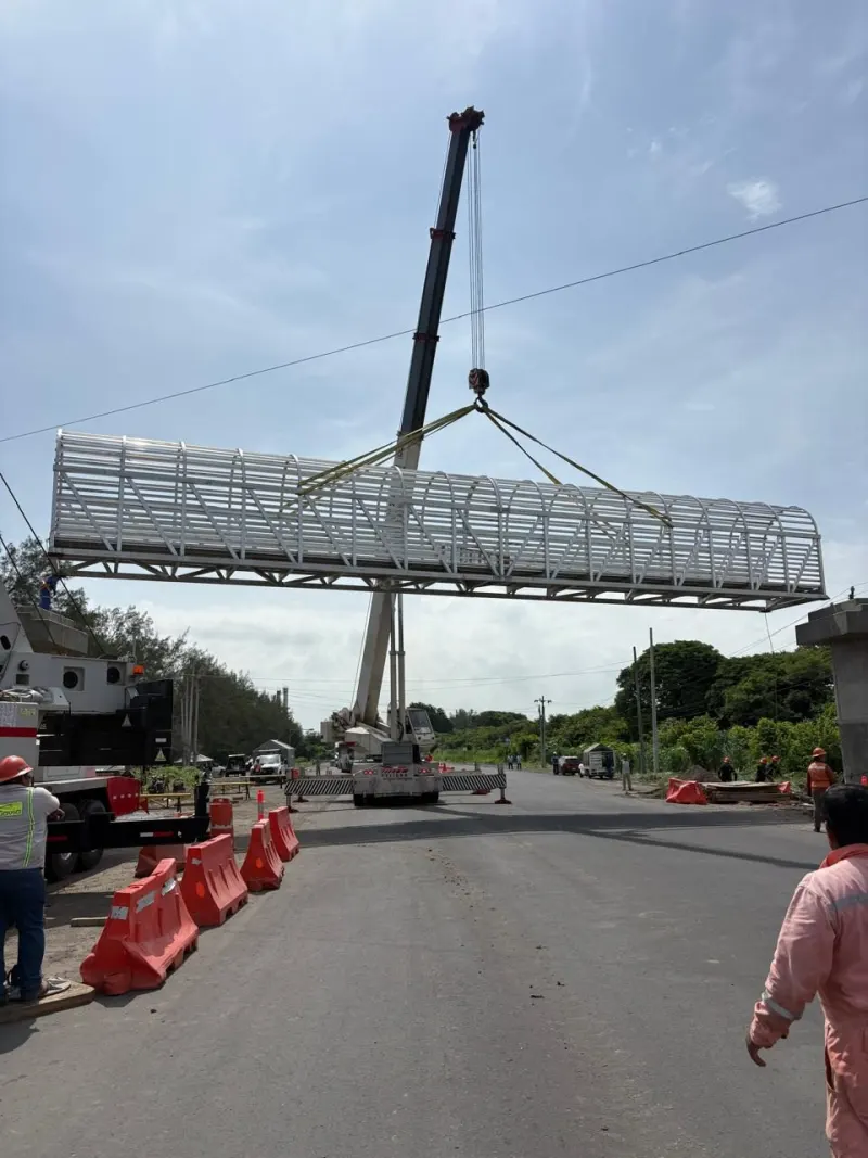 Estructura de aluminio suspendida sobre la carretera entre personal y barreras de seguridad.
