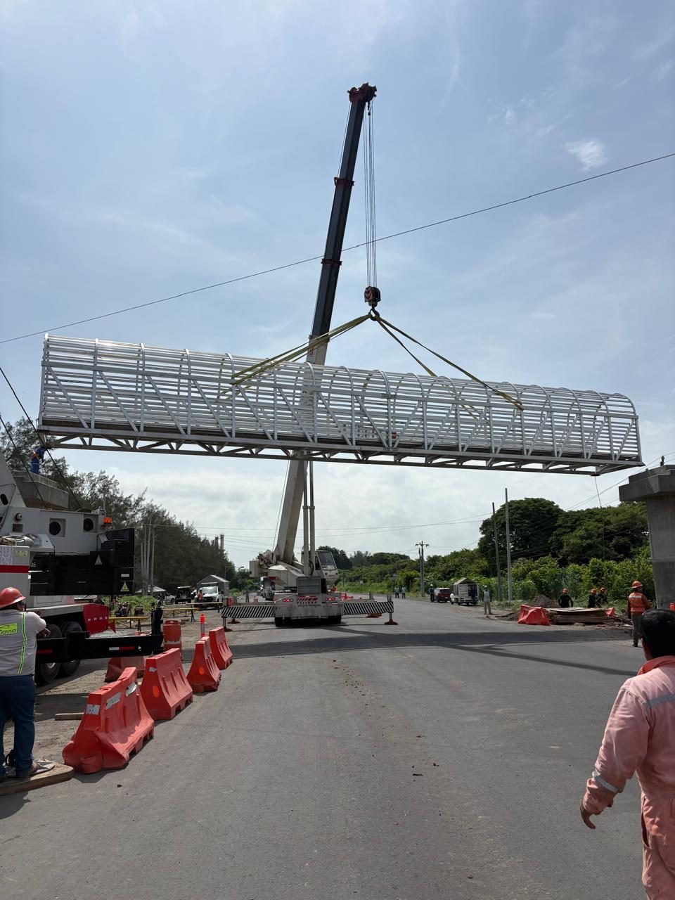 Estructura de aluminio suspendida sobre la carretera entre personal y barreras de seguridad.