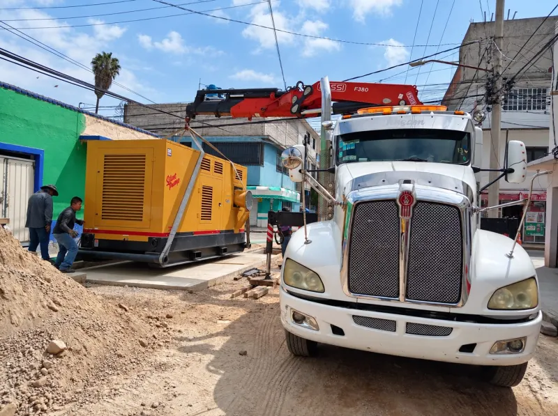Equipo amarillo con gabinete ventilado y conexión lateral, asegurado sobre un remolque de plataforma.