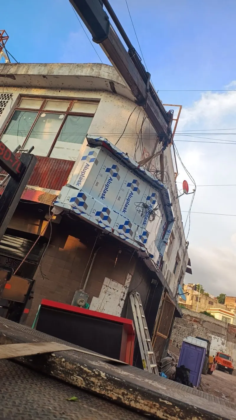 Estructura de anuncio con película protectora junto a la fachada, bajo la pluma y entre cables aéreos.