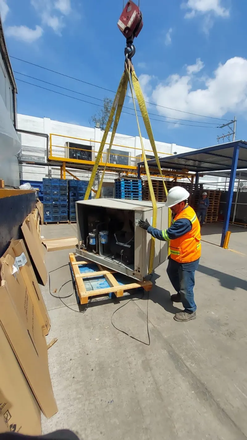 Trabajador guiando una unidad condensadora sujeta con eslingas en una zona de almacenamiento.