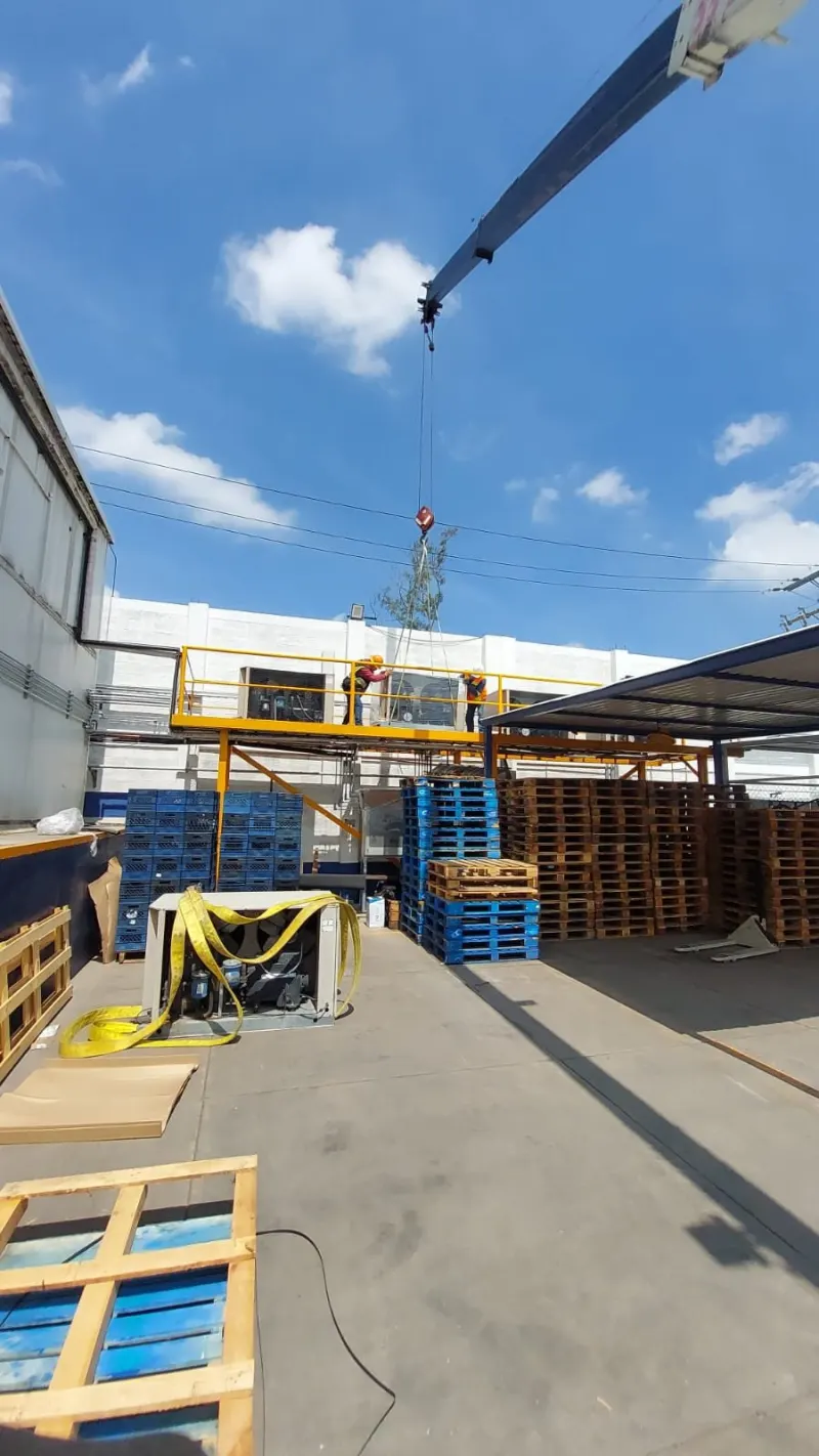 Equipo retirado en el piso, con eslingas sueltas y trabajadores sobre la plataforma elevada.