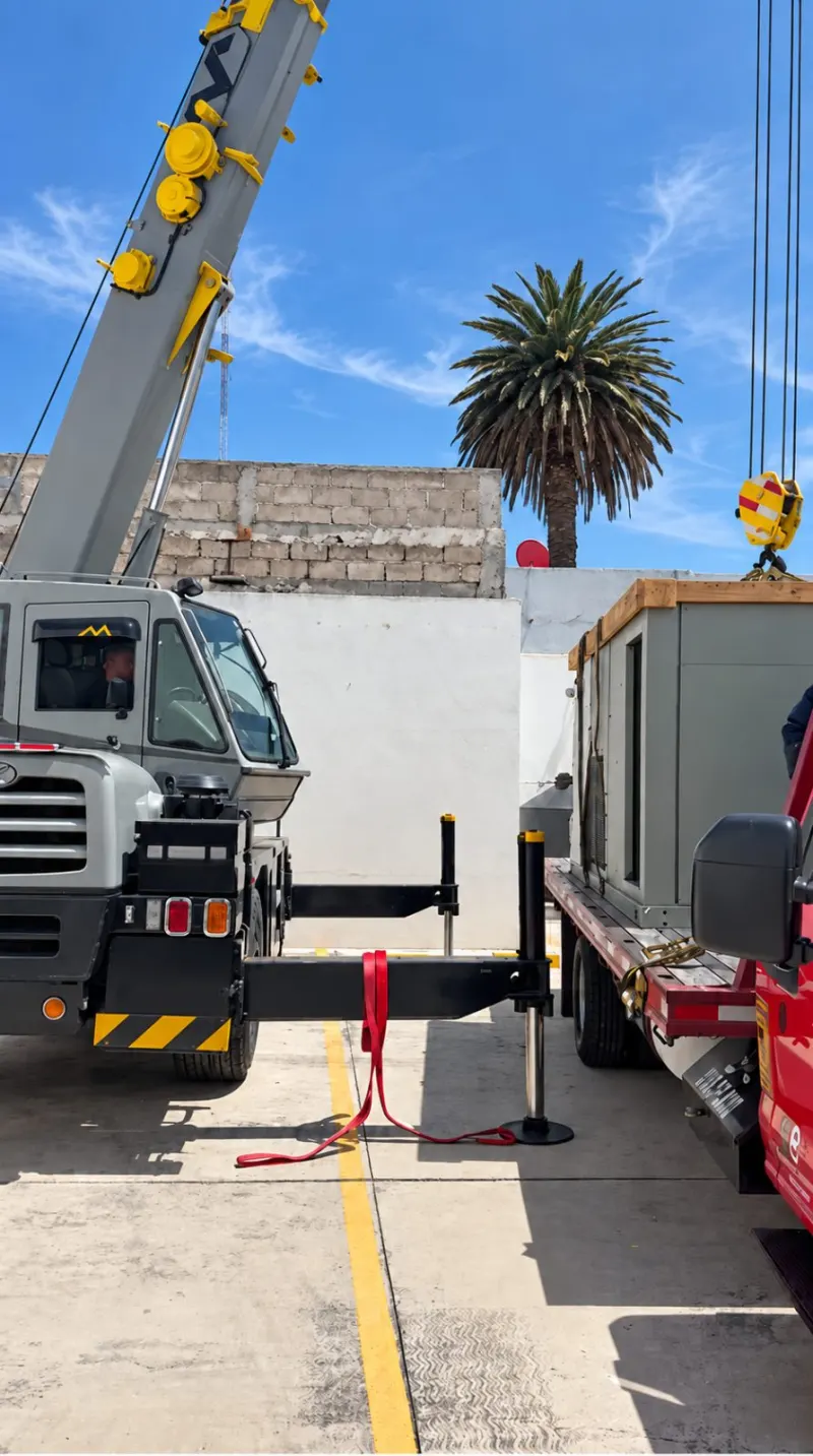 Grúa telescópica y camioneta con el paquete HVAC estacionadas dentro de un patio estrecho.