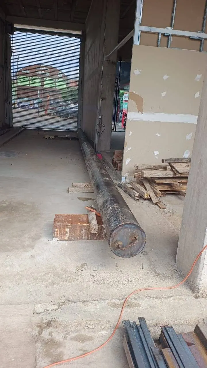 Grúa Titán verticaliza un poste metálico junto a un local, con los estabilizadores desplegados.