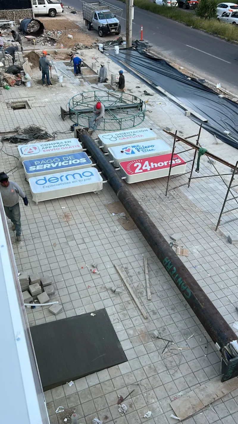 Tótem metálico tendido en el piso junto a paneles publicitarios y personal de montaje.