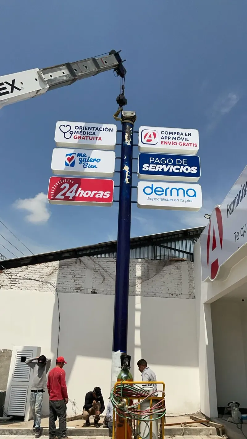 Tótem publicitario vertical suspendido por la grúa mientras personal trabaja en su base.